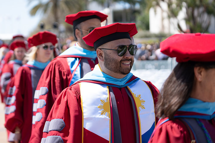 Graduate students wearing red graduation robes processing to their seats